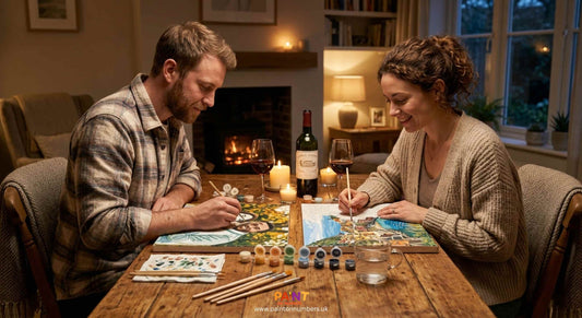 A couple sitting together at a kitchen table painting paint by numbers canvases on a relaxed date night at home