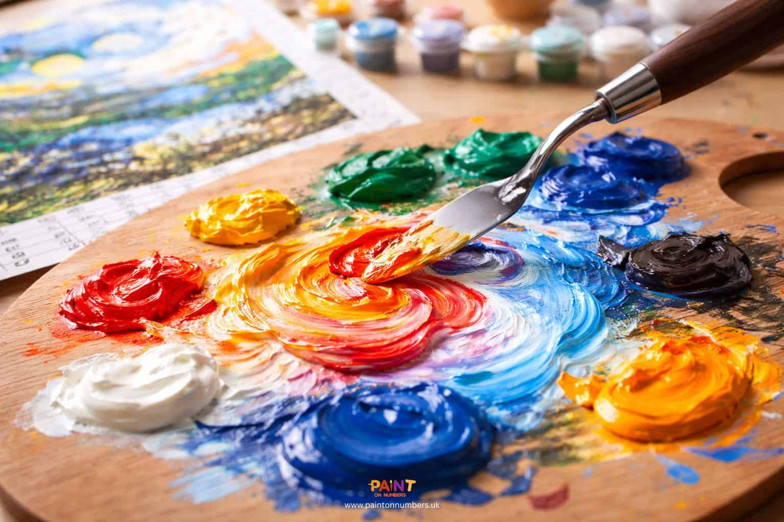 Artist mixing custom acrylic colours on a palette next to a paint by numbers canvas.