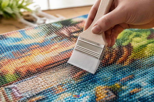 A soft brush applying clear diamond painting sealer in a thin even layer across a finished sparkling canvas