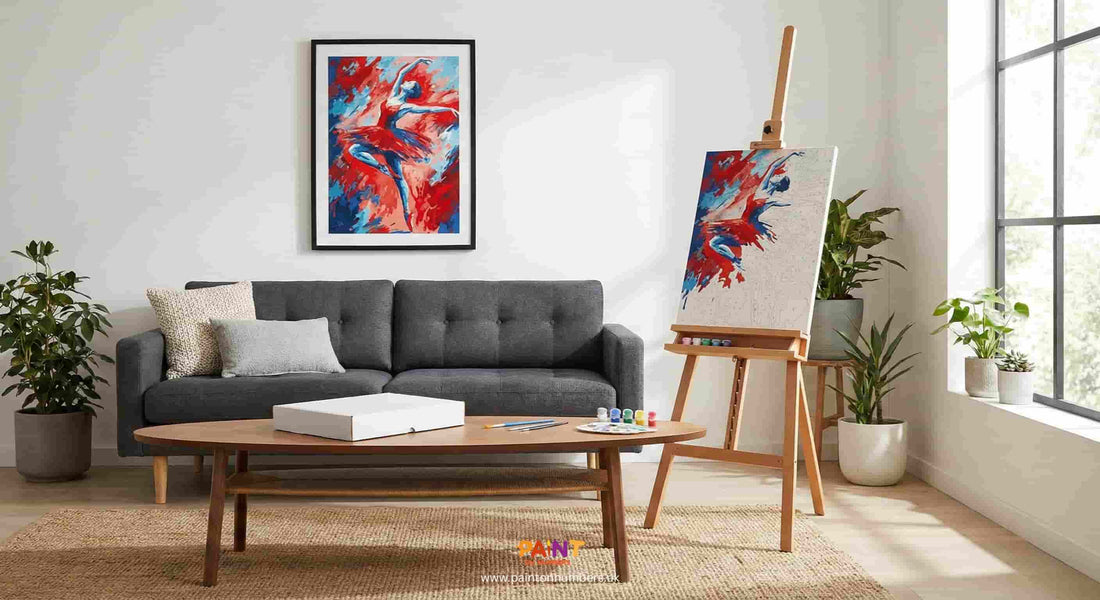 Modern living room scene featuring a framed abstract red and blue dancer Paint by Numbers art on the wall above a grey sofa. A wooden easel holds a partially completed version of the same kit with paints and brushes on a coffee table.