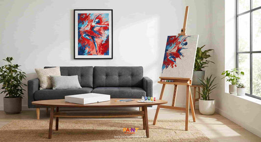 Modern living room scene featuring a framed abstract red and blue dancer Paint by Numbers art on the wall above a grey sofa. A wooden easel holds a partially completed version of the same kit with paints and brushes on a coffee table.