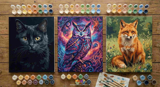 Selection of animal paint by numbers kits on a table showing completed canvases of cats, owls and wildlife designs in various styles