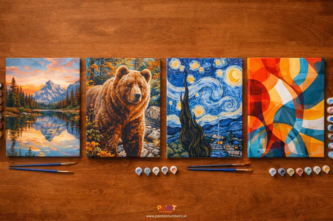Several paint by numbers kits laid out on a table showing canvases, paint pots and brushes in a comparison flat lay.