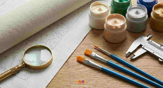 Paint containers, brushes, and a magnifying glass on a wooden surface with a map underneath.