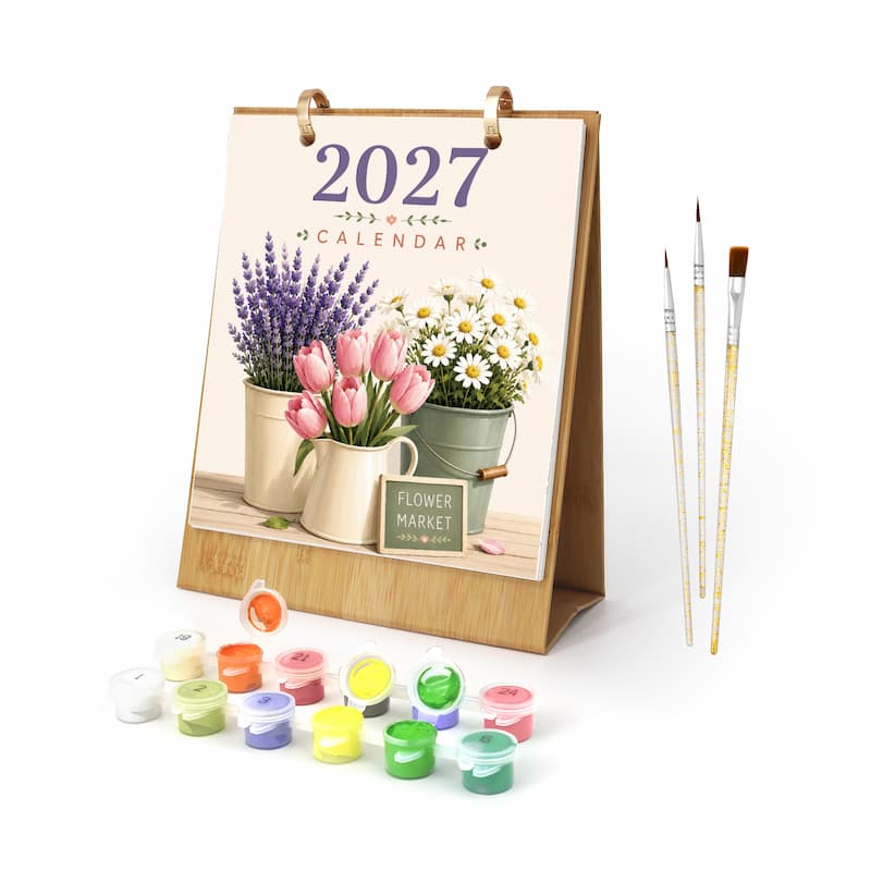A 2027 desk calendar featuring a floral market illustration with lavender, pink tulips, and white daisies, shown standing on a white background with small paint pots and three paintbrushes in front.