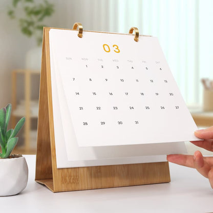 Calendar with wooden stand on a table, with a hand adjusting the page.