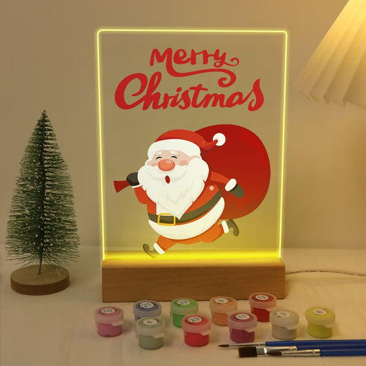 Decorative light box with Santa Claus illustration and 'Merry Christmas' text, surrounded by paint containers and a brush.
