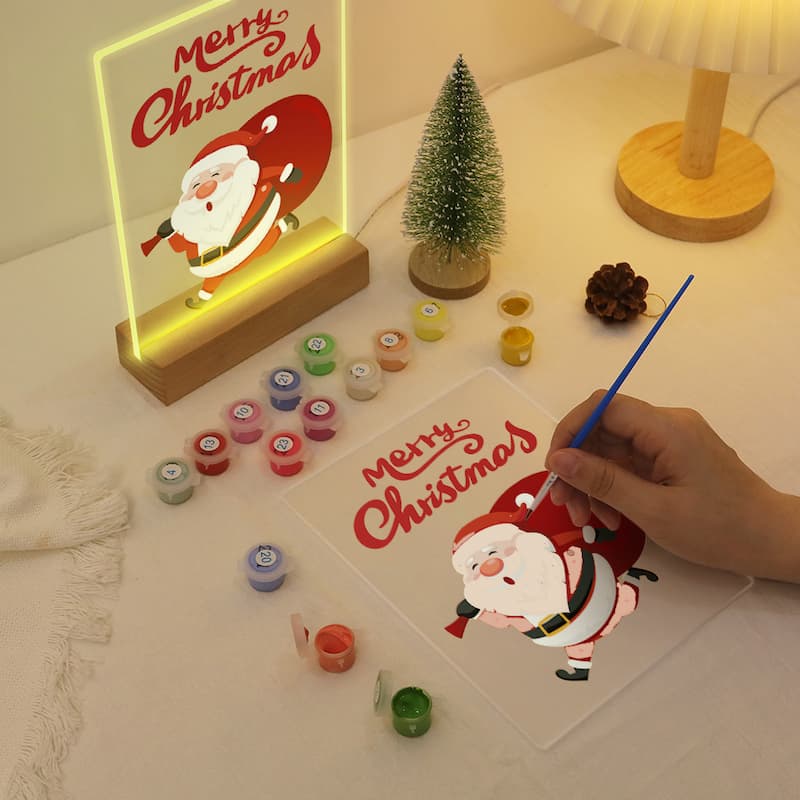 Hand painting a Christmas-themed picture with a lit 'Merry Christmas' sign in the background.