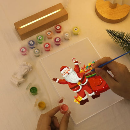 Person painting a cartoon Santa Claus on a clear acrylic block with various colors and tools.