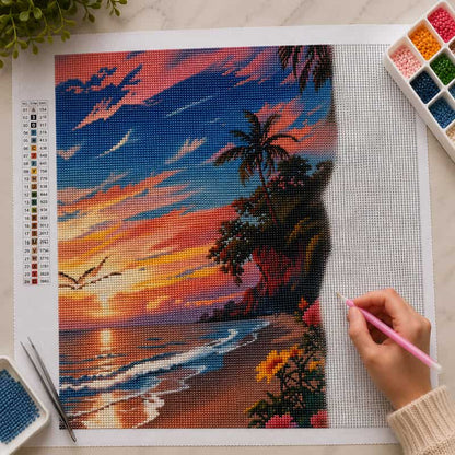 Diamond painting kit with a tropical sunset design, tools, and a hand using a pink tool.