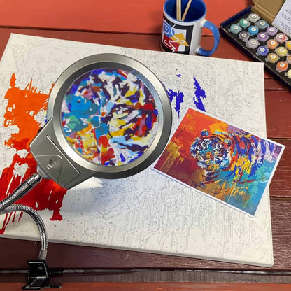 Magnifying glass over a colorful abstract painting on a wooden surface with art supplies.